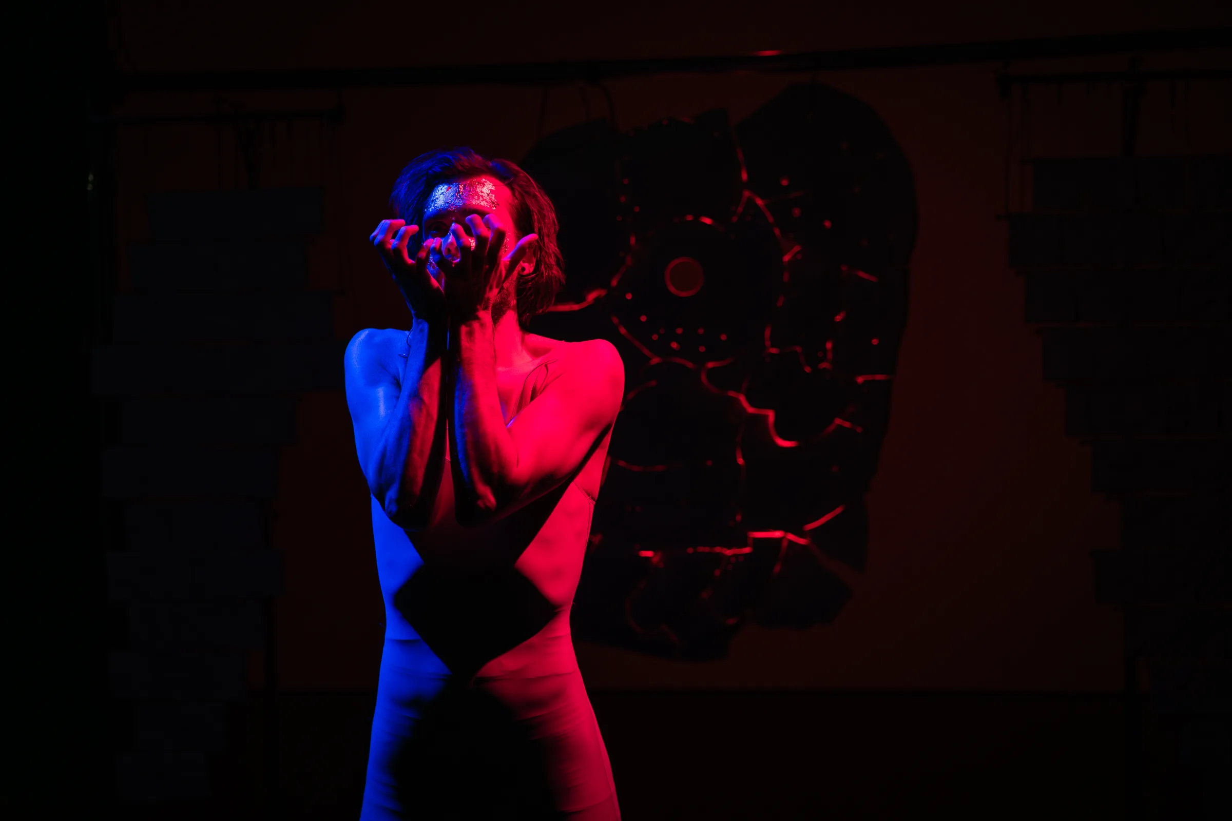 A performer faces the central ceramic sculpture in red and blue light.