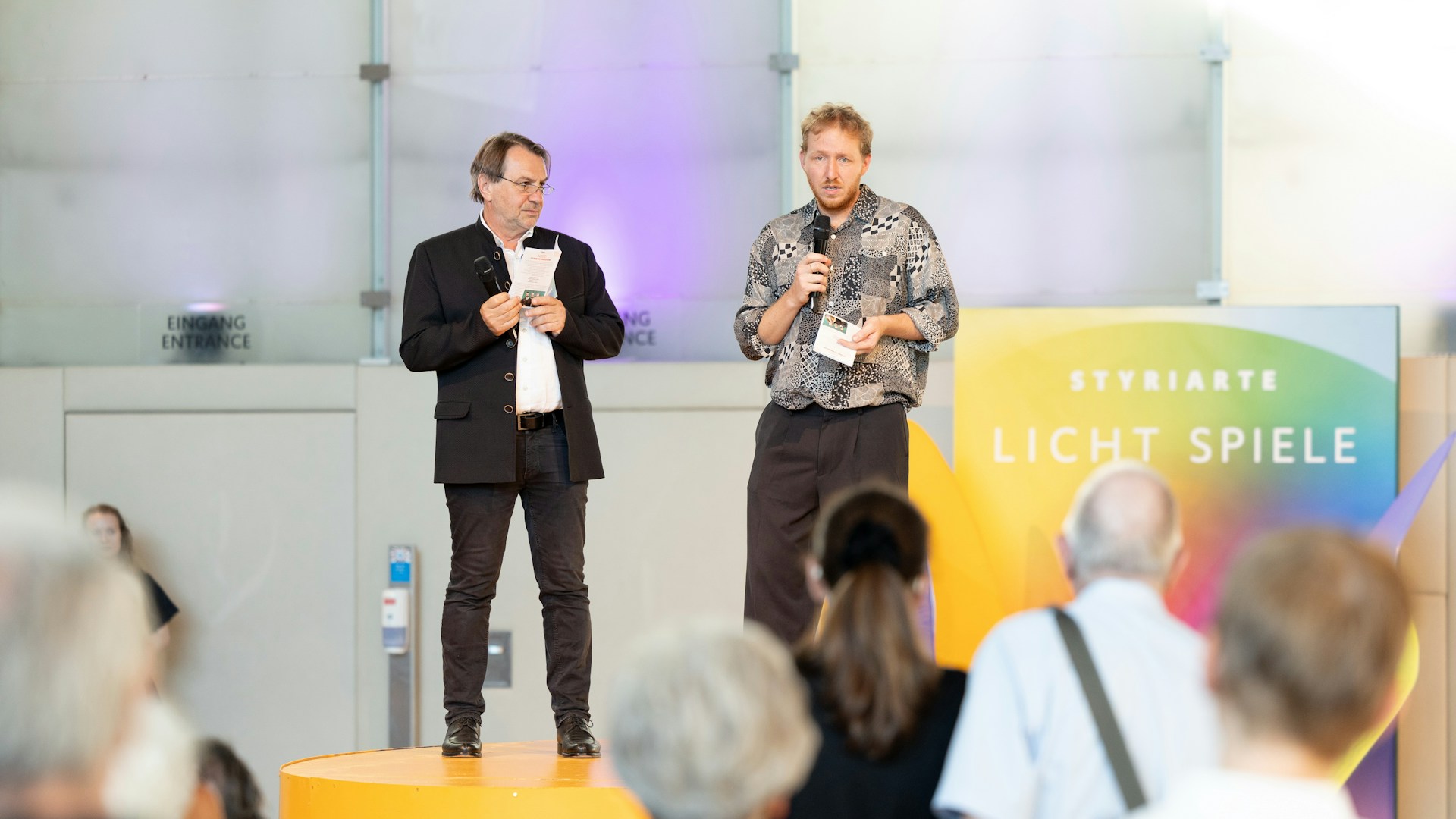 Two speakers introduce the event before a Styriarte audience in Graz.